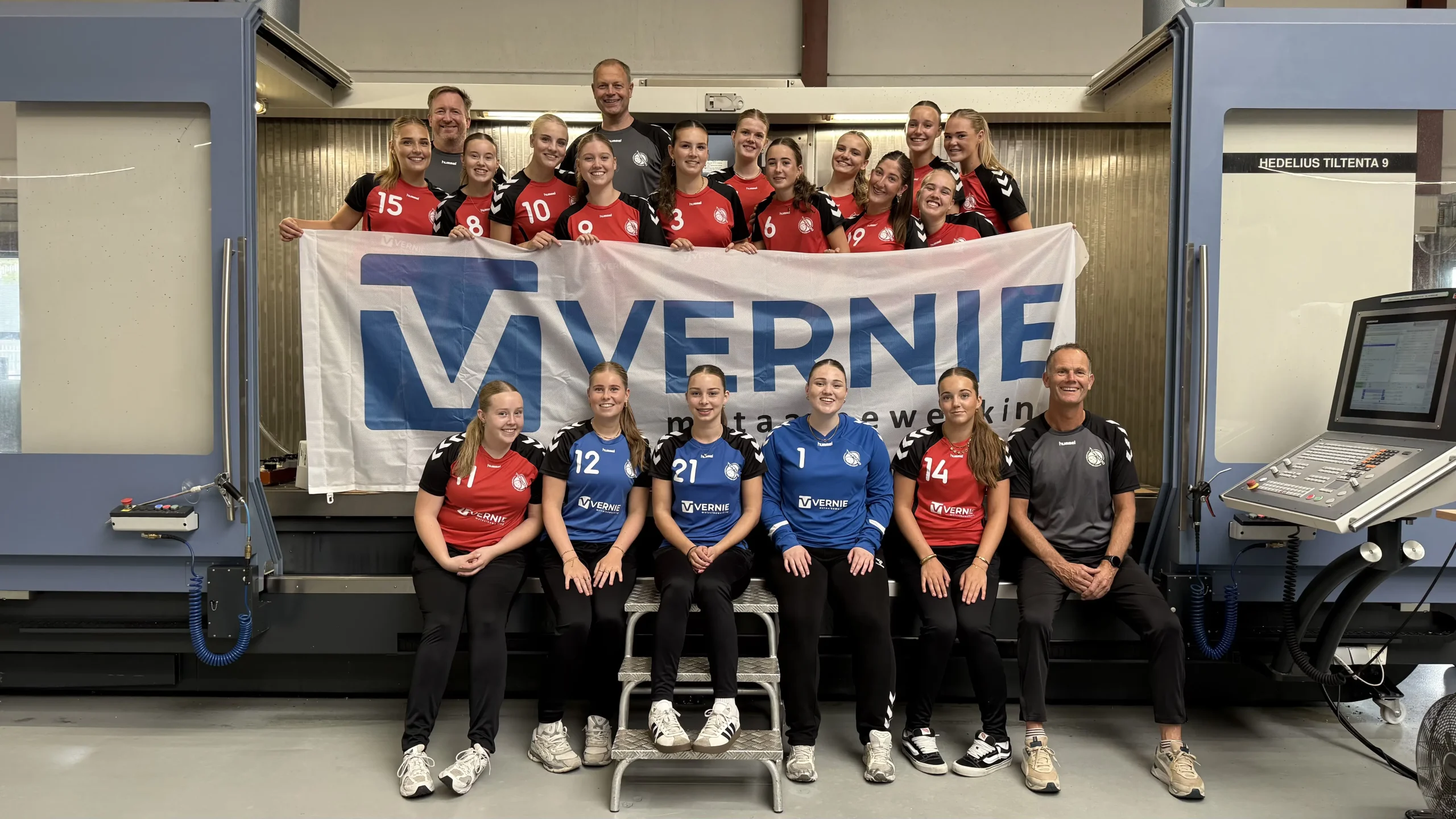 De handbaldames van HV Tornado A1 en A2 poseren in hun nieuwe gesponsorde kleding voor een CNC-machine in de werkplaats van Vernie Metaalbewerking.